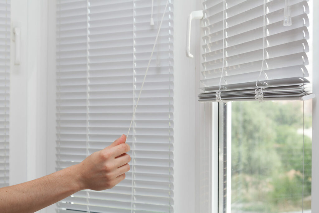 Hand raising window blinds with the cord