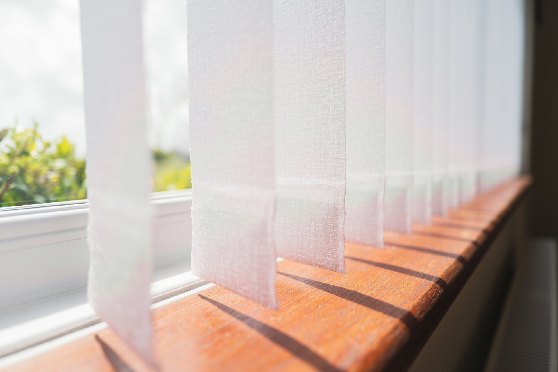 White vertical window blinds slats with sunshine peeking through.
