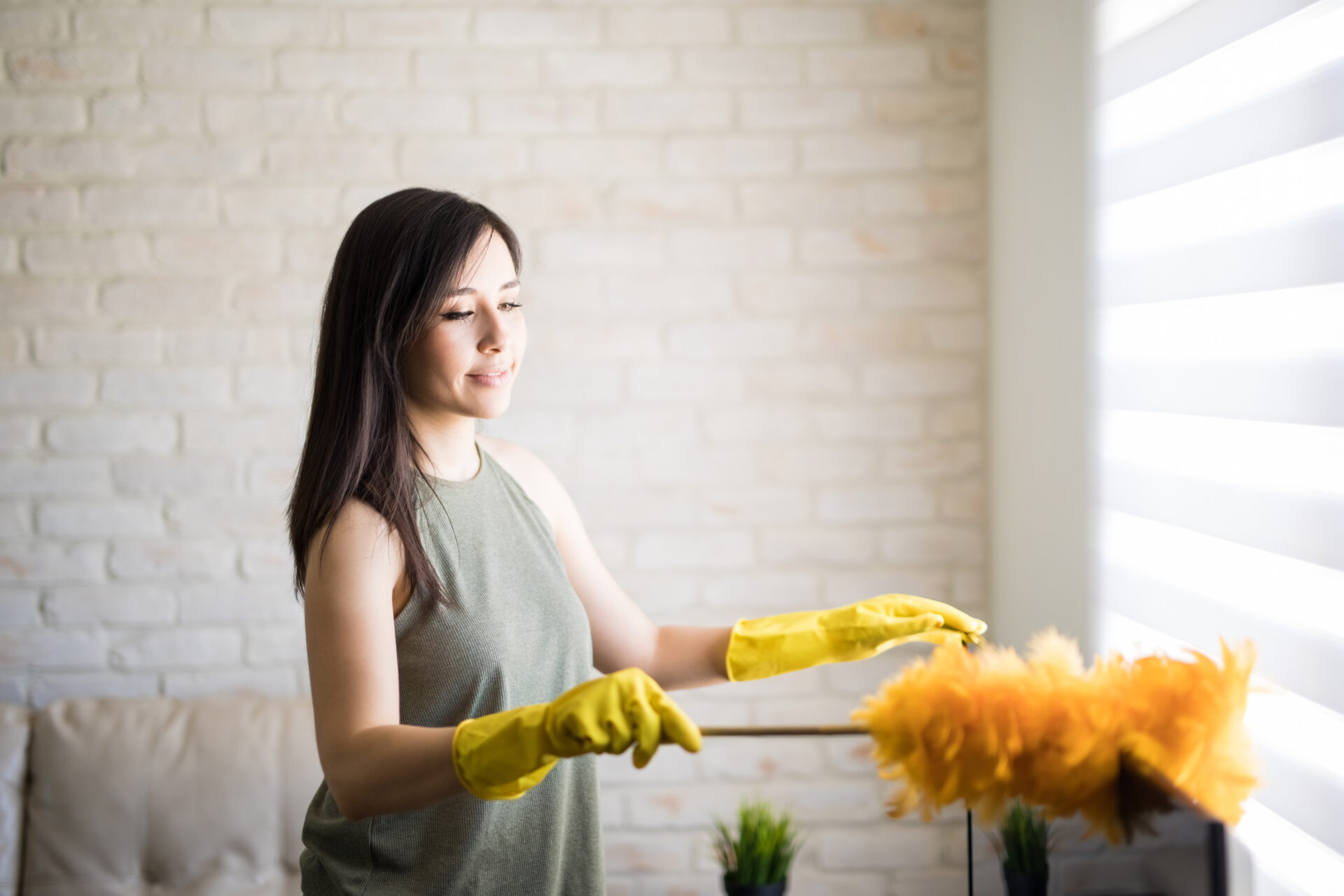 Woman dusting window blinds wearing yellow gloves with orange duster. Wholesale Blind Factory