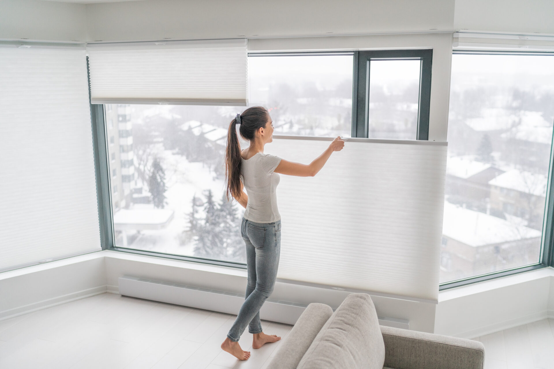 Woman opening cellular blinds in modern home. Wholesale Blind Factory